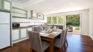 A kitchen with a dining area, wooden flooring, and a view of the outdoors. - Rodova Cottage with fireplace and enclosed backyard (Katoomba)