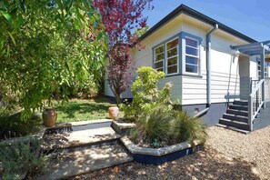 A house with a front porch, a staircase, and a garden with various plants and a tree.