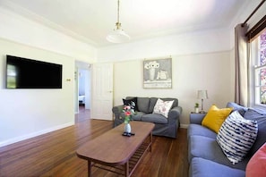A living room with a flat-screen TV, a sofa, a coffee table with a vase, and a painting on the wall.