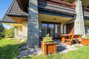 A residential building with a stone facade, a wooden deck, and outdoor furniture. - RentPlanet - Apartament Kubińca (Koscielisko)