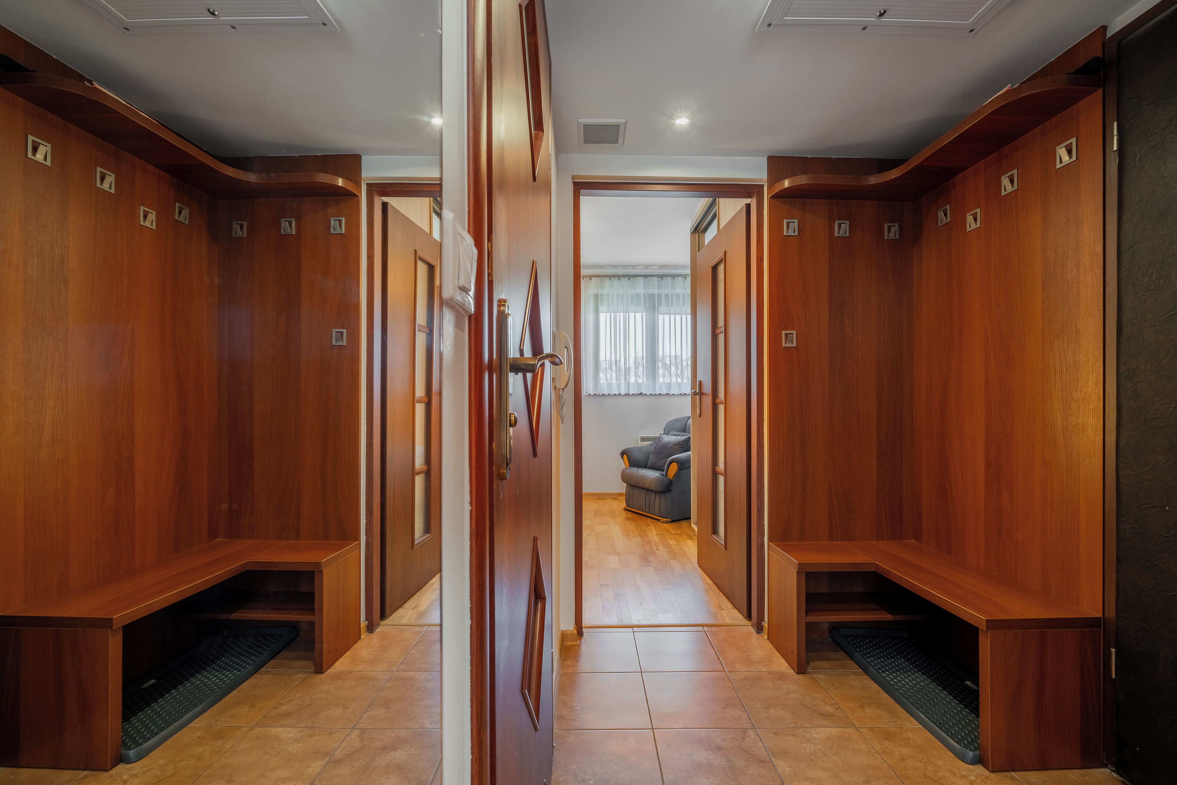 Un pasillo con paneles de madera y una puerta que da a una habitación con un sofá gris.