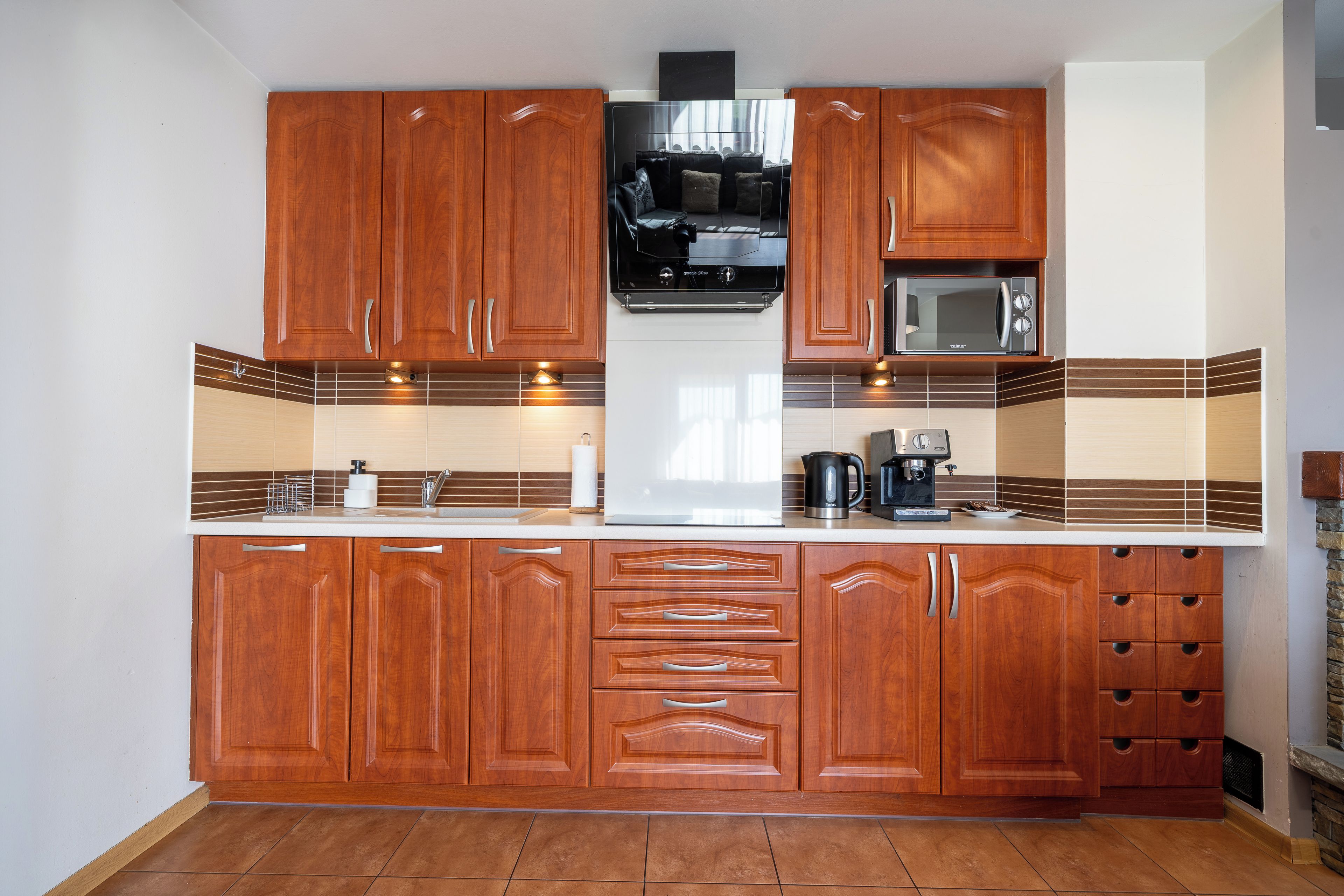 Una cocina con armarios de madera, microondas, cafetera y estufa.