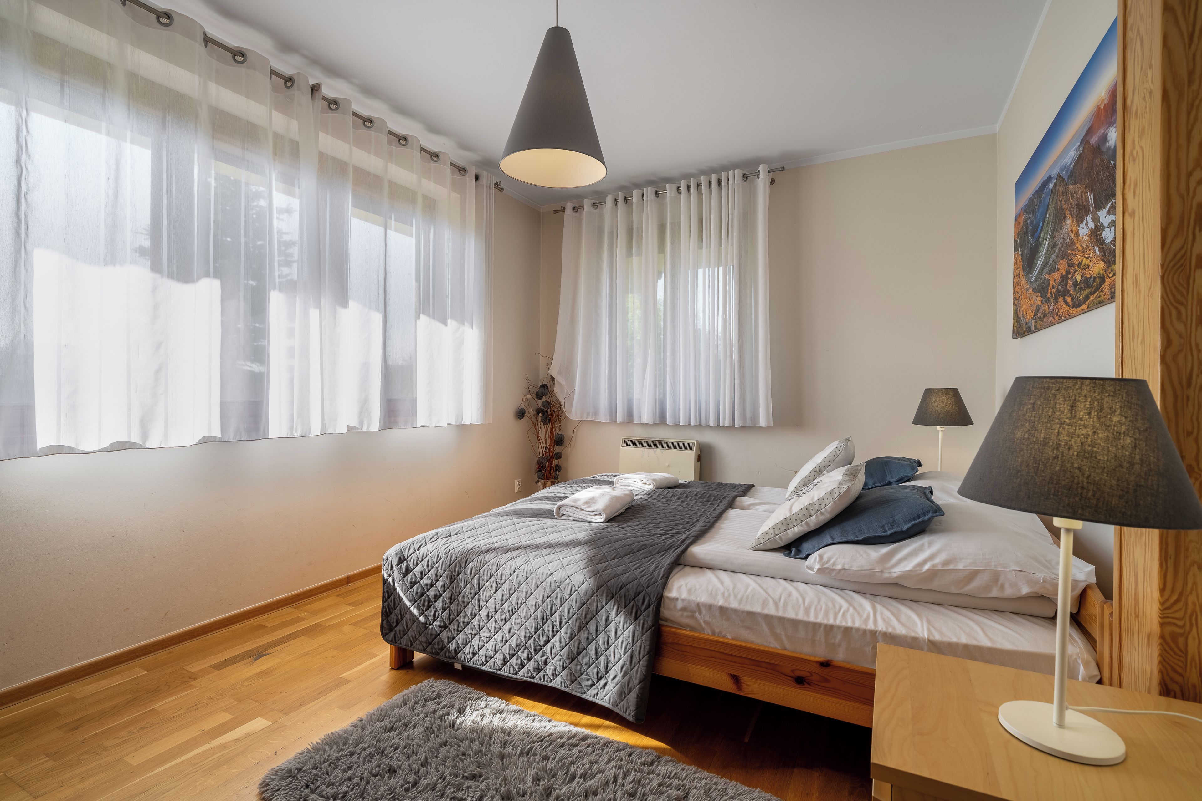 A bedroom with a bed, bedside lamps, a rug, and a painting on the wall.