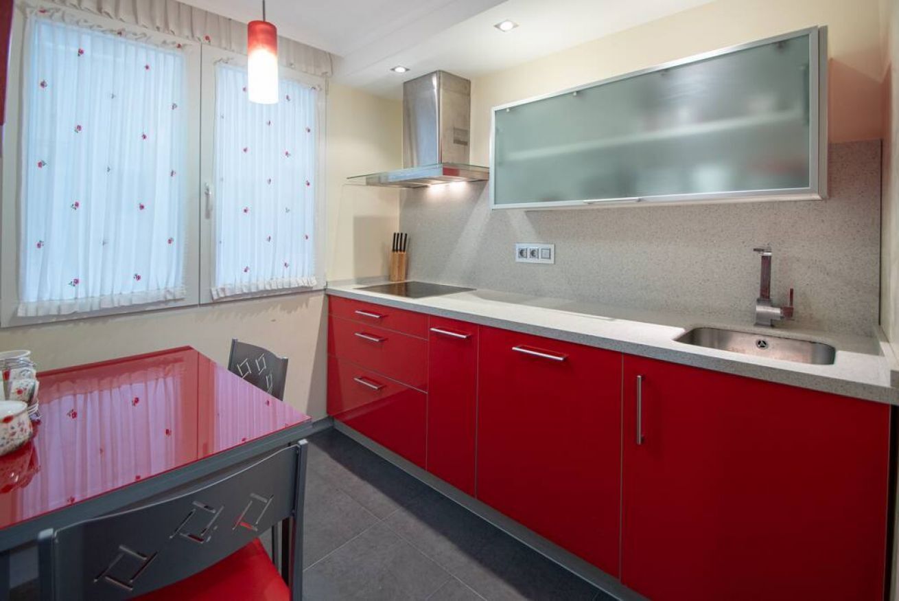 Une cuisine compacte avec des meubles rouges, un évier en acier inoxydable et un luminaire suspendu moderne.