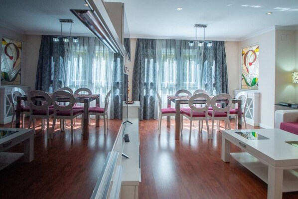 A modern dining area with white tables and chairs, large windows with sheer curtains, and abstract artwork on the walls.