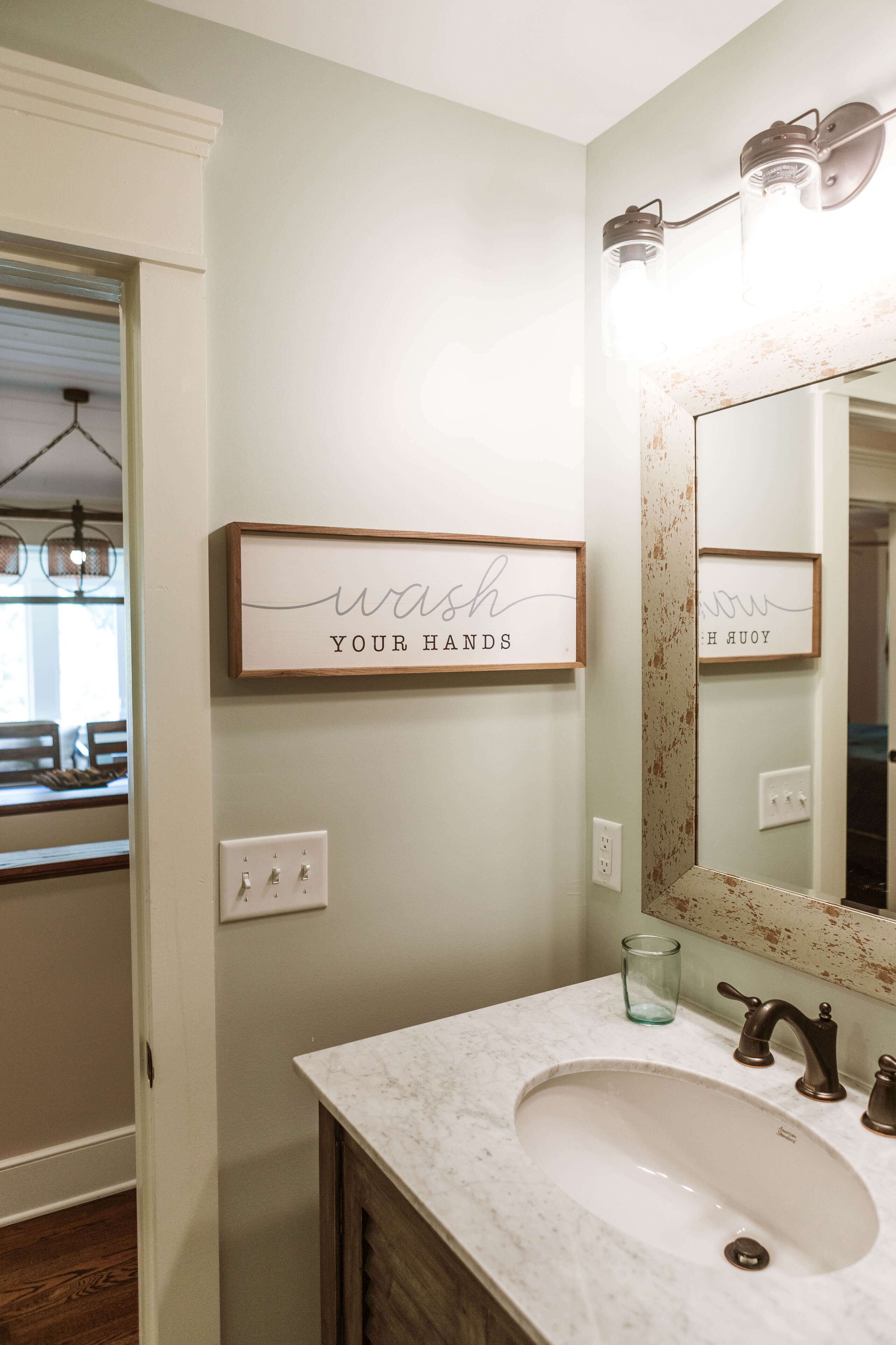 Un baño con lavabo de mármol, un espejo con marco decorativo y un cartel que dice 'lávate las manos'.