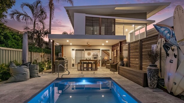 A modern house with a swimming pool, outdoor seating, and a surfboard decoration.
