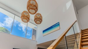 A modern interior with a staircase, large windows, and a beach-themed painting.