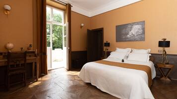 A hotel room with a large bed, wooden flooring, a desk with a globe, and a view of the outdoors.
