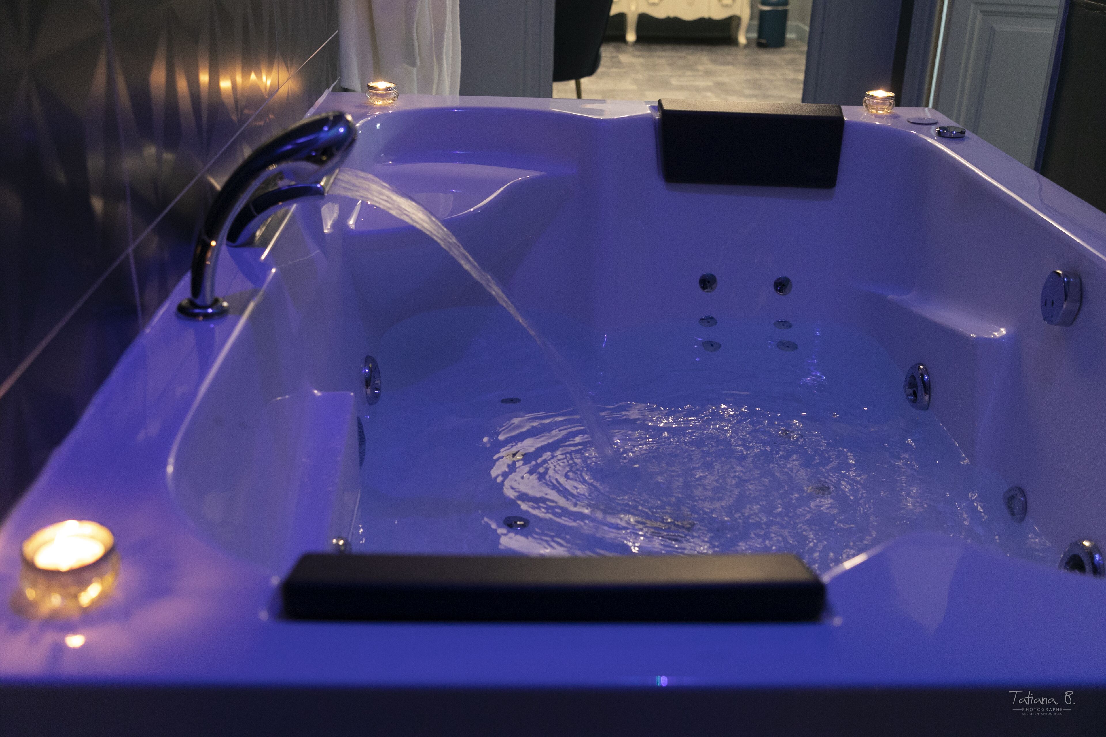 A modern bathroom with a large bathtub, a handheld showerhead, and a small candle on the edge.