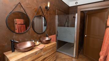 Un baño con tocador de madera, dos espejos redondos, un lavabo de cobre y una cabina de ducha de vidrio.