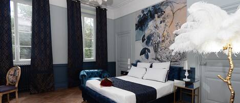 Un dormitorio con una cama grande, cortinas azul oscuro, una araña y un cuadro floral de gran tamaño en la pared.