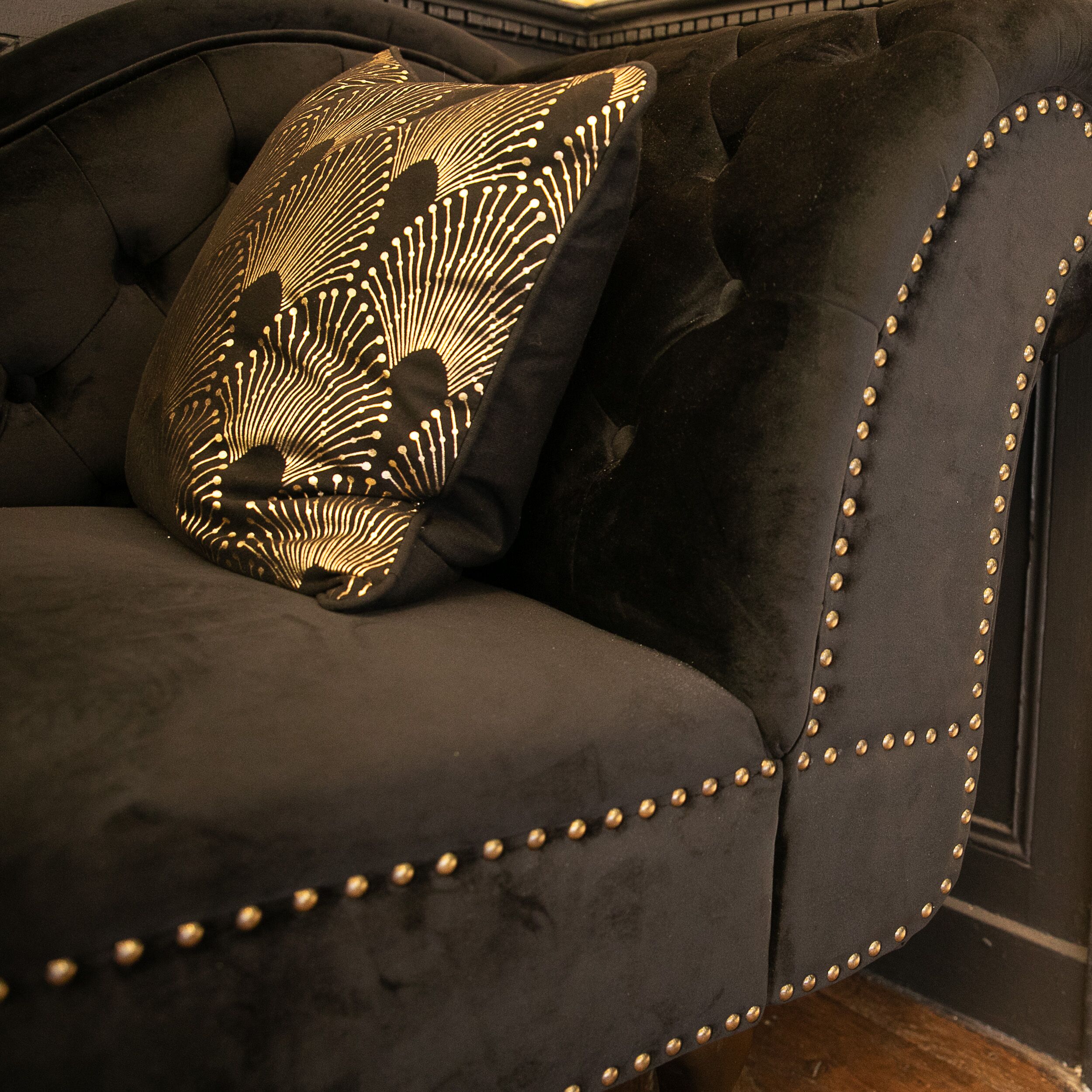 Ein dunkel gepolstertes Sofa mit goldenen Nieten und einem gemusterten Kissen.