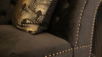 Ein dunkel gepolstertes Sofa mit goldenen Nieten und einem gemusterten Kissen.