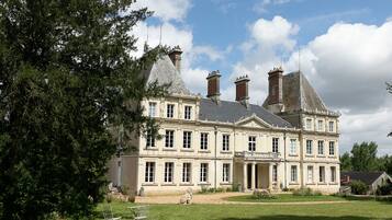 Un edificio grande e histórico con varias chimeneas, un césped cuidado y una estatua en primer plano.