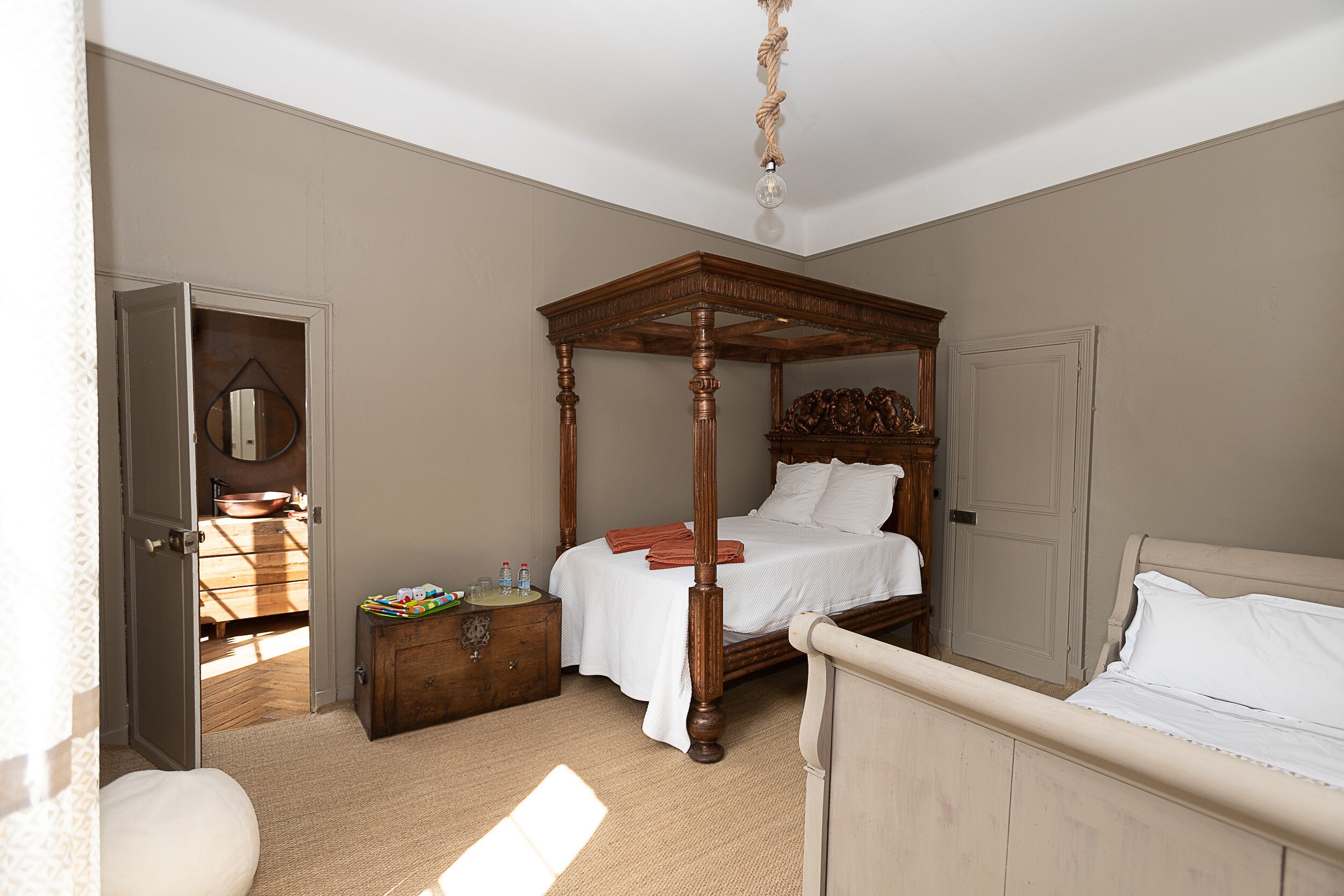 A four-poster bed with a wooden canopy, a bedside table with a mirror, and a door leading to a bathroom.