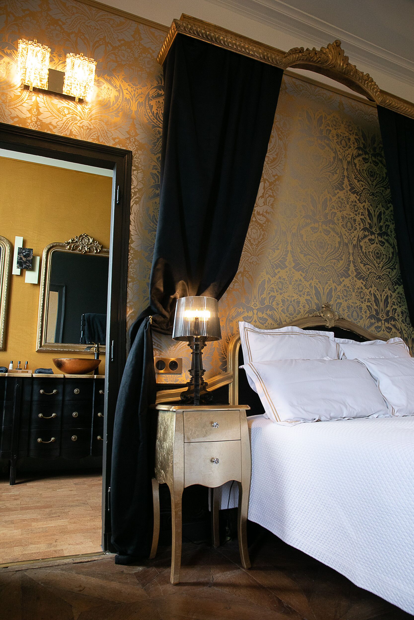 Une chambre à coucher avec un lit, une table de chevet avec une lampe, une commode, un miroir et un rideau.