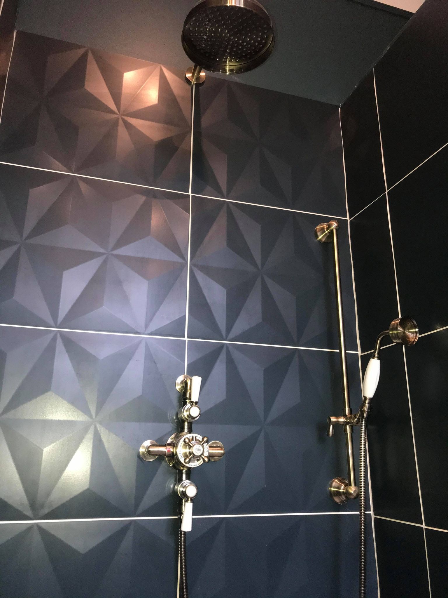 Een badkamer met een wand met een geometrisch patroon, een douchekop en een handdouche.