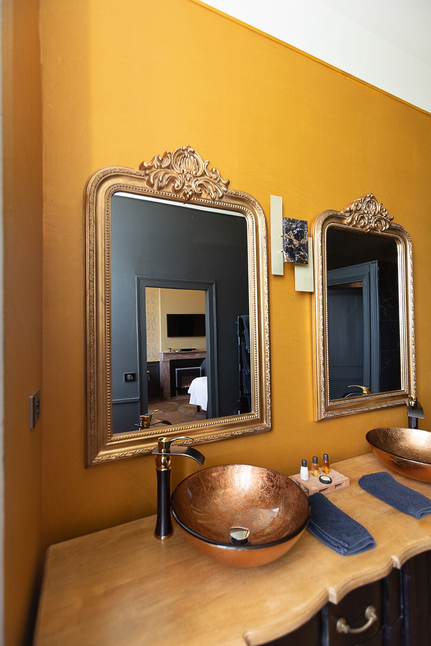 Une salle de bain avec deux grands miroirs, un lavabo en cuivre et un meuble-lavabo en bois.