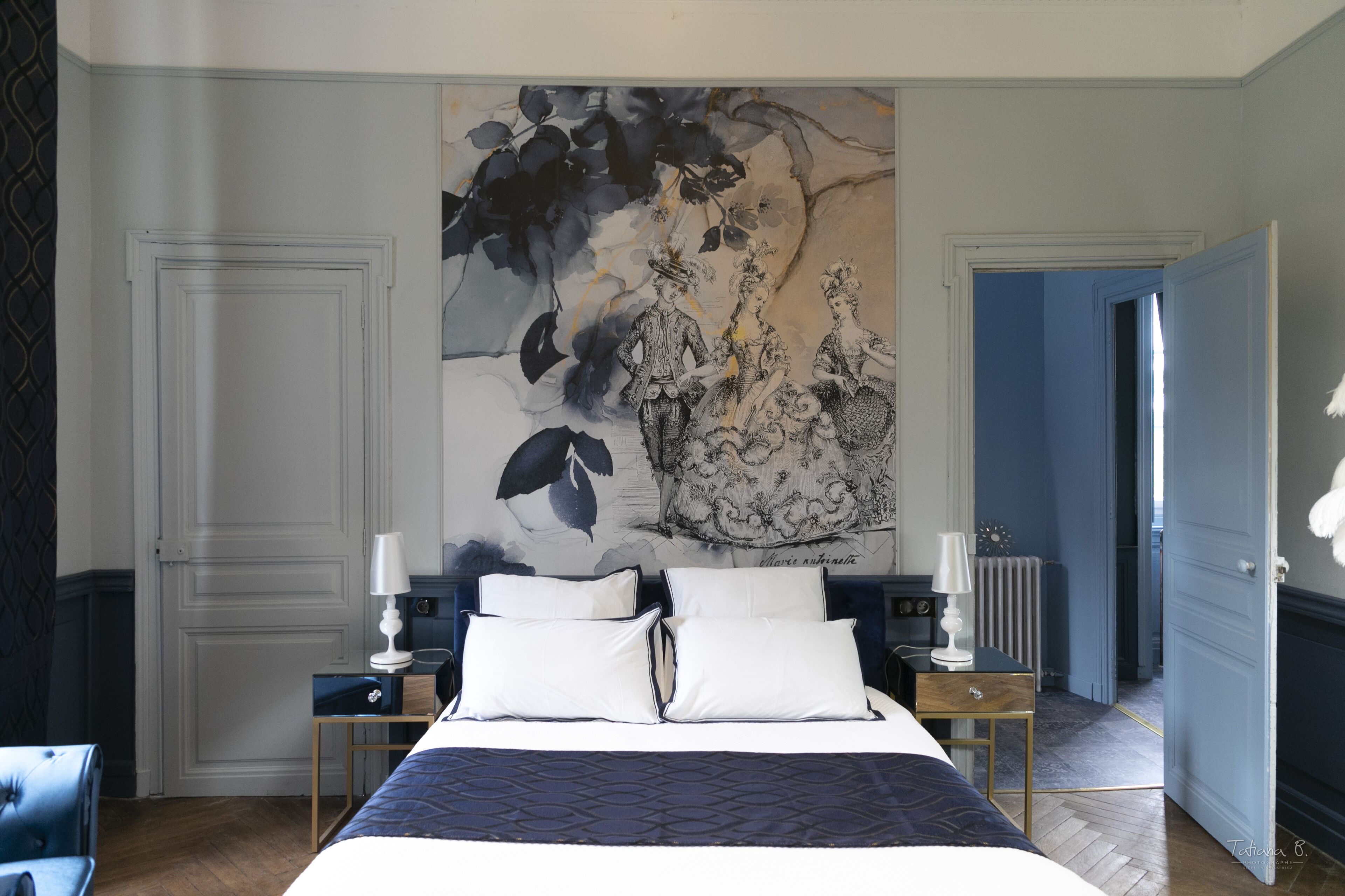 A bedroom with a large bed, two bedside tables with lamps, a large floral artwork on the wall, and a view of the hallway.