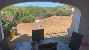 Une terrasse avec une table et des chaises, un pot de fleurs et une vue sur un espace aménagé avec des arbres et des arbustes.