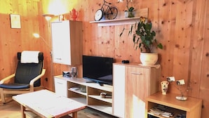 Une pièce chaleureuse avec un décor intérieur en bois, une chaise noire, un téléviseur, un bureau et une bibliothèque.