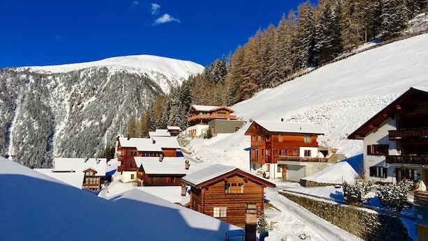 Un village de montagne enneigé, avec des chalets en bois et un ciel d’un bleu limpide.