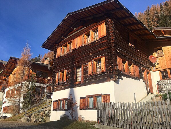 A traditional wooden chalet with a sloped roof, wooden shutters, and a white exterior wall.
