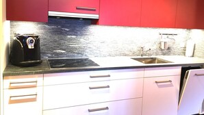 Une cuisine moderne avec des meubles de rangement rouges, une machine à café, un évier et un robinet en acier inoxydable.