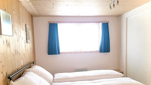 Une chambre avec un lit superposé, des murs en bois, une fenêtre avec des rideaux bleus et un petit radiateur.