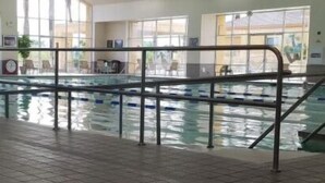 Une piscine intérieure dotée d’un sol carrelé, de rampes en métal et de grandes fenêtres laissant entrer la lumière naturelle.