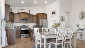 A kitchen with wooden cabinets, stainless steel appliances, and a dining area with white chairs and a table. - Rock Canyon Oasis 4 Bedroom Home by RedAwning (Washington)
