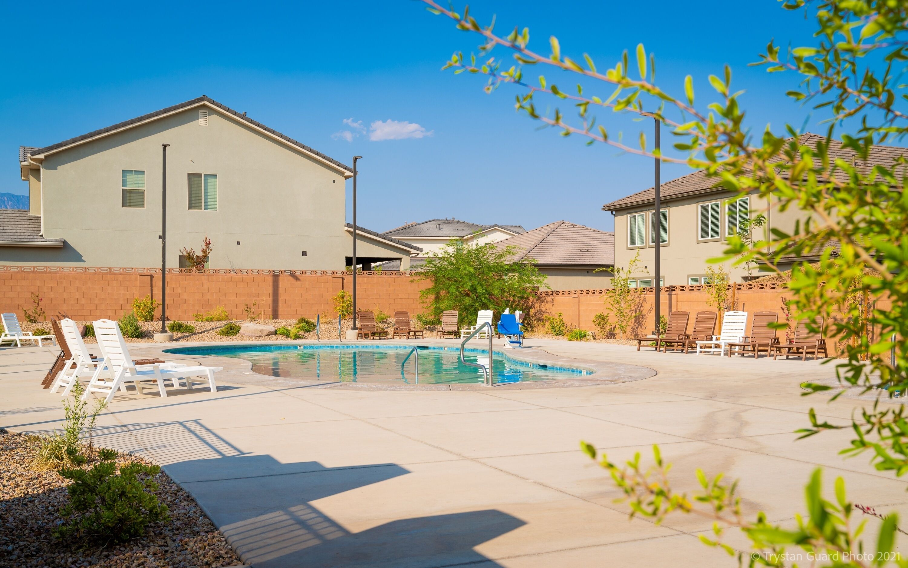 A residential area with a swimming pool, lounge chairs, and a brick wall.