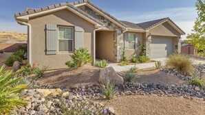 A two-story house with a sloped roof, a garage, and a landscaped front yard with rocks and desert plants. - Rock Canyon Oasis 4 Bedroom Home by RedAwning (Washington)