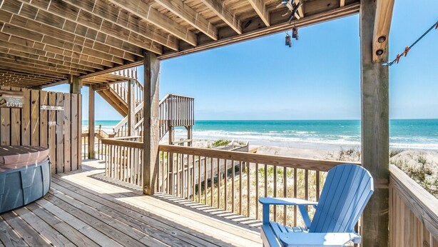 A wooden deck with a view of the ocean, a wooden staircase, and a blue Adirondack chair.