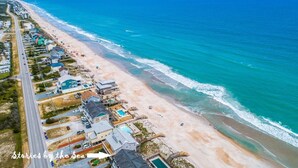 An aerial view of a coastal area with a beach, houses, and a road.