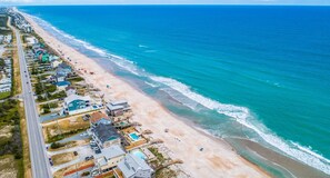 Une vue aérienne d’une zone côtière avec une plage, des maisons et une route.
