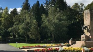 Un parco con un monumento commemorativo, un vialetto lastricato e una panchina.