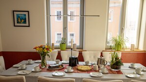 Un tavolo da pranzo apparecchiato con piatti, tazze e una torta, circondato da sedie, con vista dalla finestra e un quadro appeso al muro.