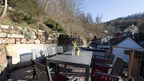 Una terrazza esterna con tavolo e sedie, un muro in pietra e vista sulle case sullo sfondo.