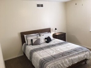 Un dormitorio con cama, mesita de noche, lámpara y ventana.