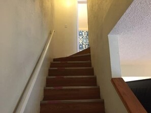 Un escalier en bois, doté d’une rampe, mène à une pièce dont la fenêtre est ornée de motifs.