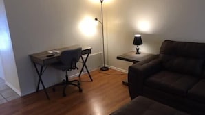 Une pièce avec un plancher en bois, un bureau avec une chaise, une lampe et un canapé marron.