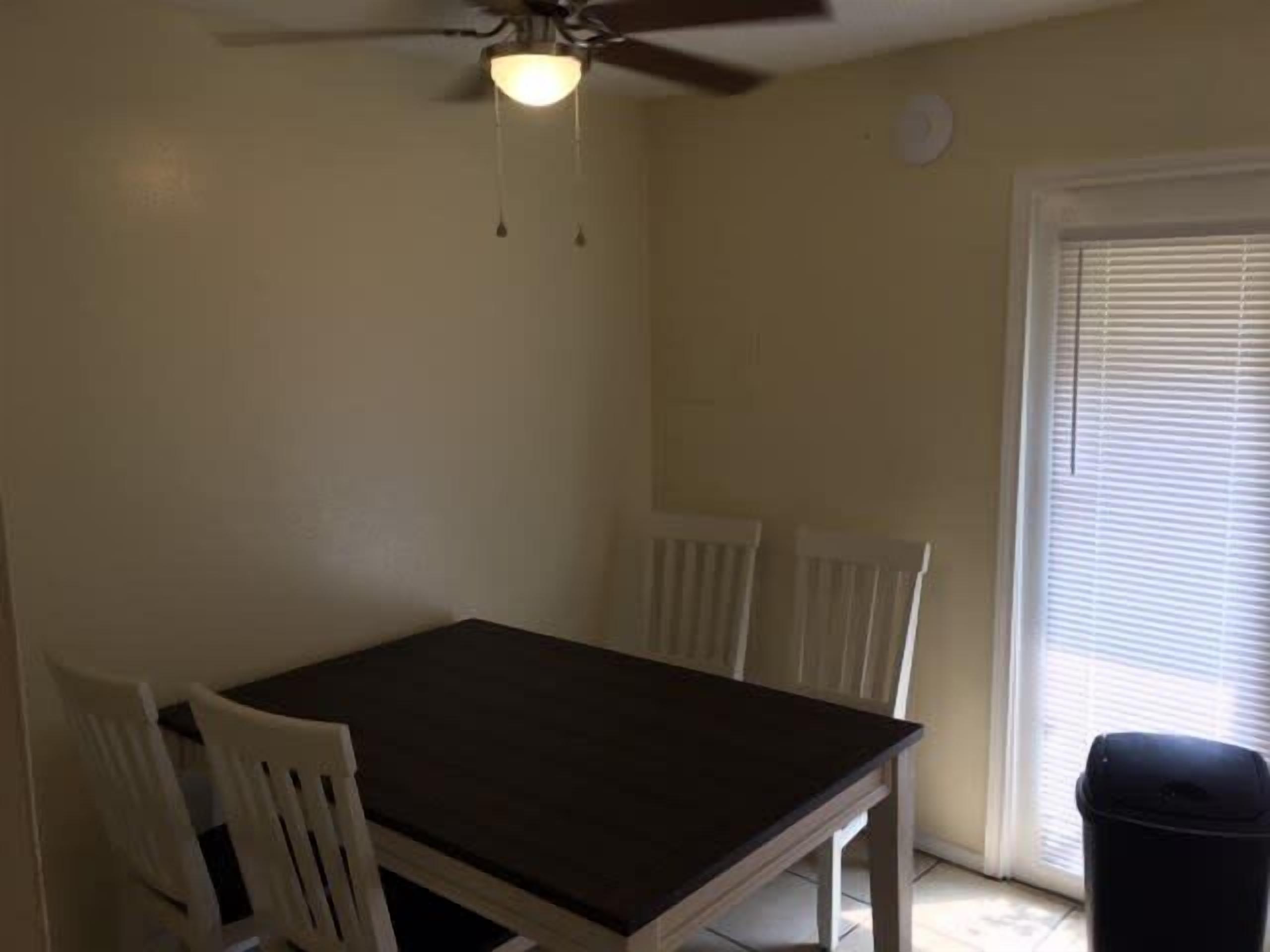 A dining area with a table and chairs, a ceiling fan, and a window with blinds.