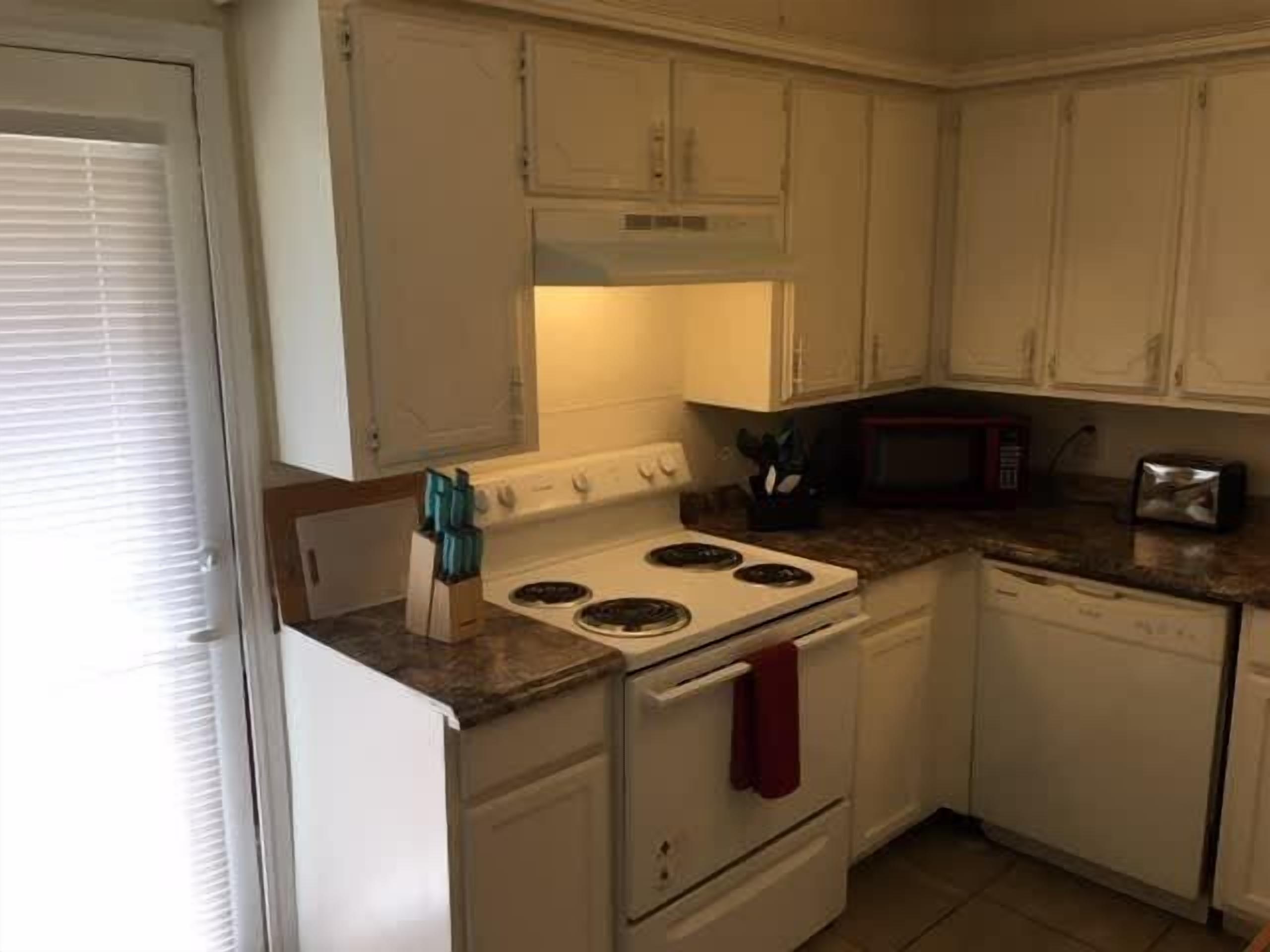 A kitchen with white cabinets, a stove, a microwave, and a toaster.