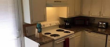 A kitchen with white cabinets, a stove, a microwave, and a toaster.