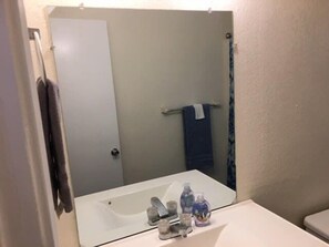 Un baño con lavamanos blanco, espejo y toallero.