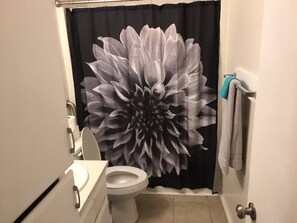 A bathroom with a large floral shower curtain, a toilet, and a sink. - Two-bed one-bath downstairs close to Fort Sill! (Lawton)