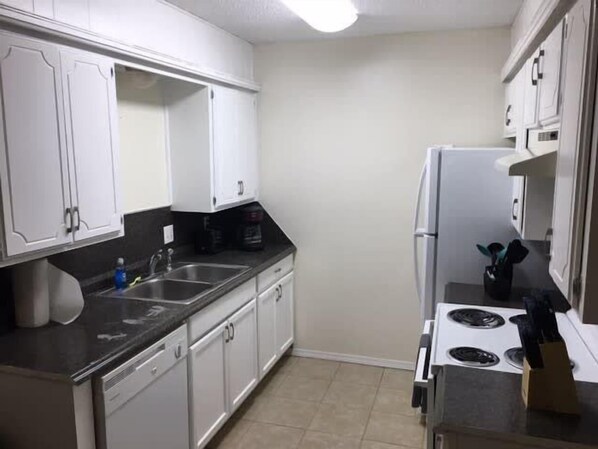 Una cocina compacta con armarios blancos, encimera negra, refrigerador blanco y estufa.