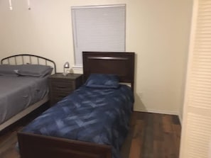 A bedroom with two beds, a nightstand, and a window with blinds. - Two-bed one-bath downstairs close to Fort Sill! (Lawton)